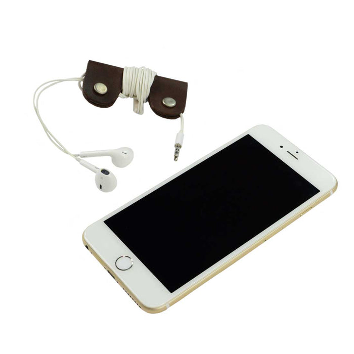The Wrap Cord Keeper by Hide & Drink displayed alongside a smartphone, illustrating its functionality as a cable organizer holder. Made from full grain leather, this handmade accessory is crafted in small batches in La Antigua Guatemala & Oaxaca Mexico.